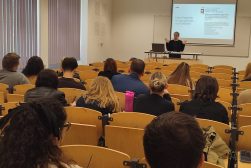Dr Aleksandra Gawrysiak-Zabłocka w auli wykładowej podczas wykładu na Wydziale Prawa Pan-European University (Paneurópska vysoká škola) w Bratysławie. Na pierwszym planie słuchacze, w tle Pani dr. stojąca przed ekranem, na którym wyświetlono prezentację.