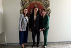Dr Magdalena Maksymiuk w trakcie stażu na Uniwersytecie Wileńskim. Zdjęcie grupowe wraz z dwiema innymi badaczkami, na tle godła uczelni. Pani dr. po lewej stronie.