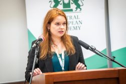 Prelegentka przemawia przy mównicy między dwoma mikrofonami, na tle baneru Central European Academy