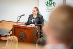 Małgorzata Burzyńska przemawia przy mównicy z godłem Uniwersytetu Kardynała Stefana Wyszyńskiego w Warszawie, przed banerem Central European Academy i uczestnikami wydarzenia.
