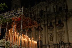 Nocna procesja religijna: ozdobny baldachim z płonącymi świecami i białymi kwiatami na tle fasady zabytkowego kościoła