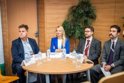 Cztery osoby uczestniczące w panelu, w tym prof. Muszyński siedzą przy okrągłym stole z wizytówkami, butelkami wody i szklankami.