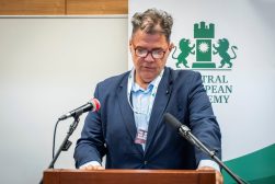 Prof. UKSW dr hab. Marcin Muszyński przemawia przy mównicy między dwoma mikrofonami, na tle baneru Central European Academy