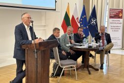 Mężczyzna przemawia przy mównicy podczas panelu; obok siedzą czterej uczestnicy, a w tle widoczne są flagi Litwy, Polski, Unii Europejskiej i NATO.