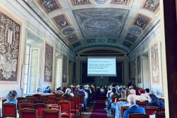 Uczestnicy konferencji siedzą w zabytkowej sali z ozdobnym sklepieniem i oglądają prezentację wyświetlaną na ekranie