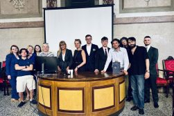 Grupa uczestników wydarzenia pozuje przy dużym drewnianym stole w reprezentacyjnej sali z dekoracyjnymi ścianami